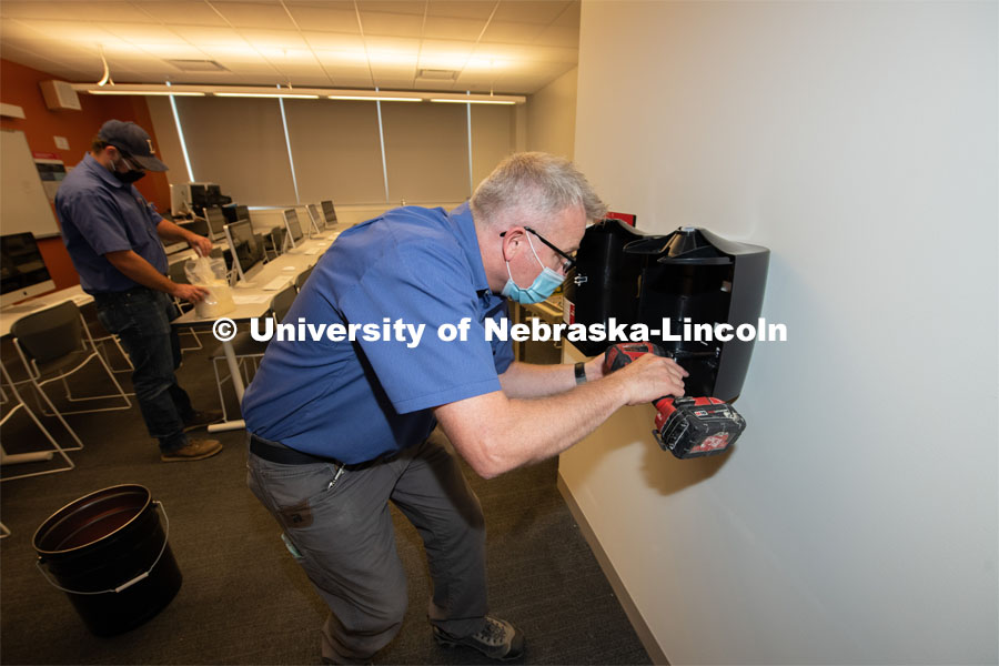 Matt Rivers and Jackson Kelly of Building Systems Maintenance install hand sanitizer, disinfectant wipes, paper towels, trash cans and floor coverings in classrooms across campus. August 11, 2020. Photo by Gregory Nathan / University Communication.